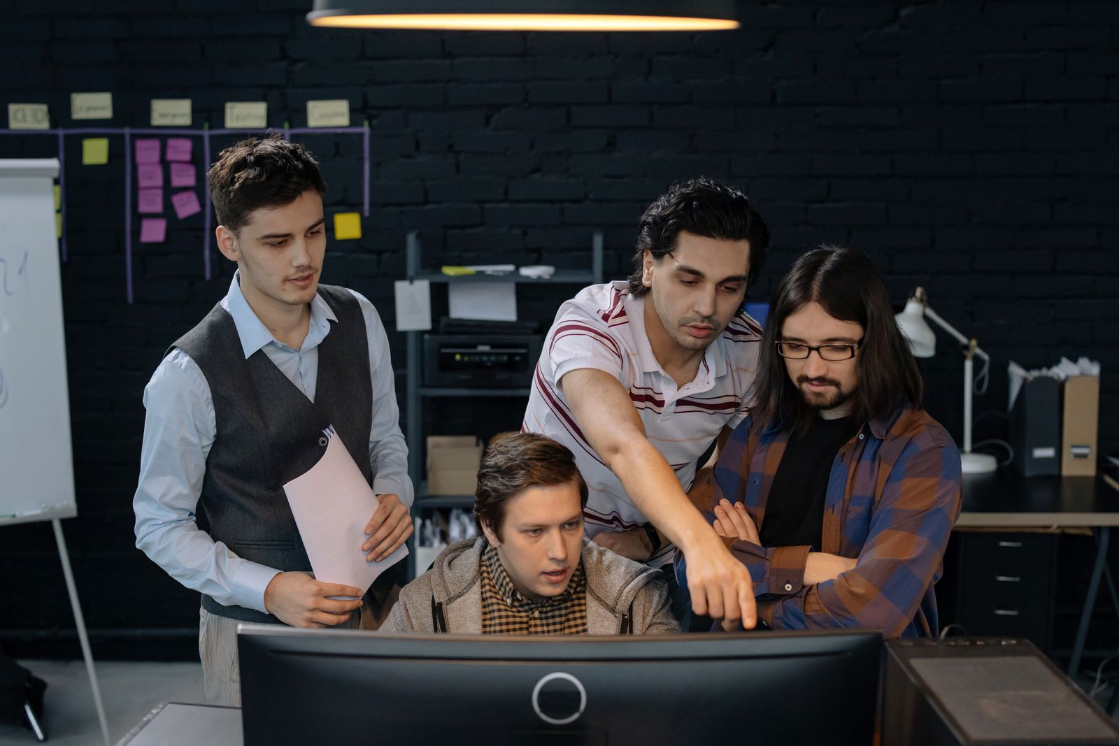Four developers gathered around one monitor, one pointing at the screen